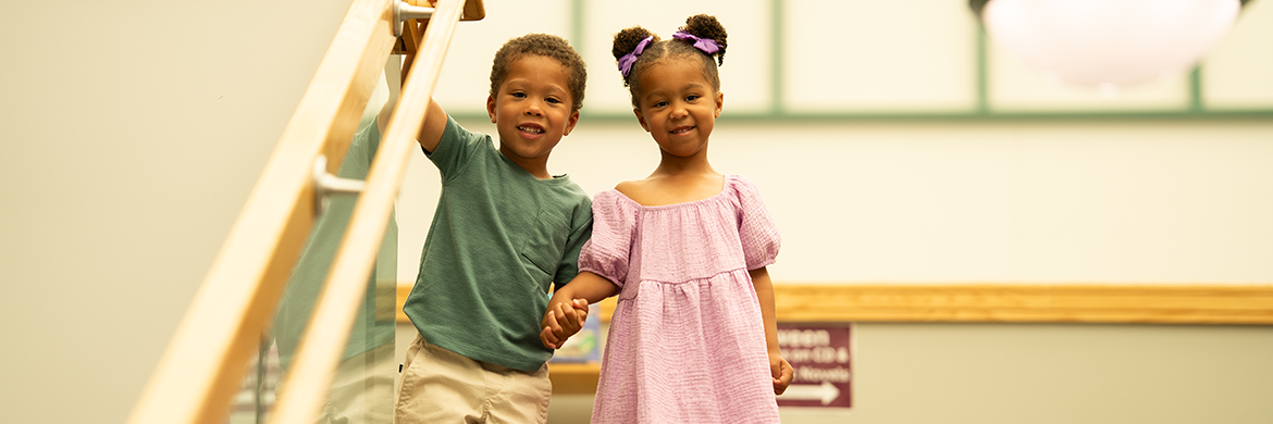 A boy and a girl smiling side-by-side inside the library