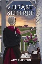"A Heart Set Free" book cover showing an amish woman standing on a porch next to a desk with a flower arrangement.  She is shown from behind and she is looking toward a road with a horse and buggy and a farm in the distance. 