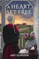 "A Heart Set Free" book cover showing an amish woman standing on a porch next to a desk with a flower arrangement.  She is shown from behind and she is looking toward a road with a horse and buggy and a farm in the distance. 