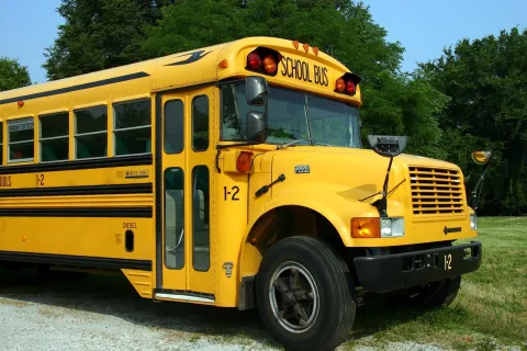 Front end of yellow school bus with trees and grass in the background