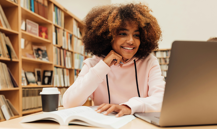 Teen girl smiling while working on a laptop in the library